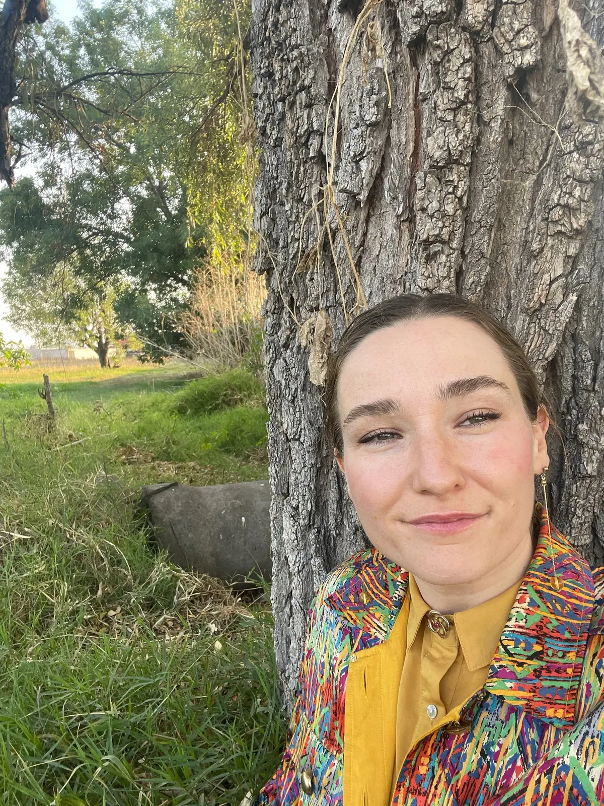 Sarah smiling, leaning against a tree