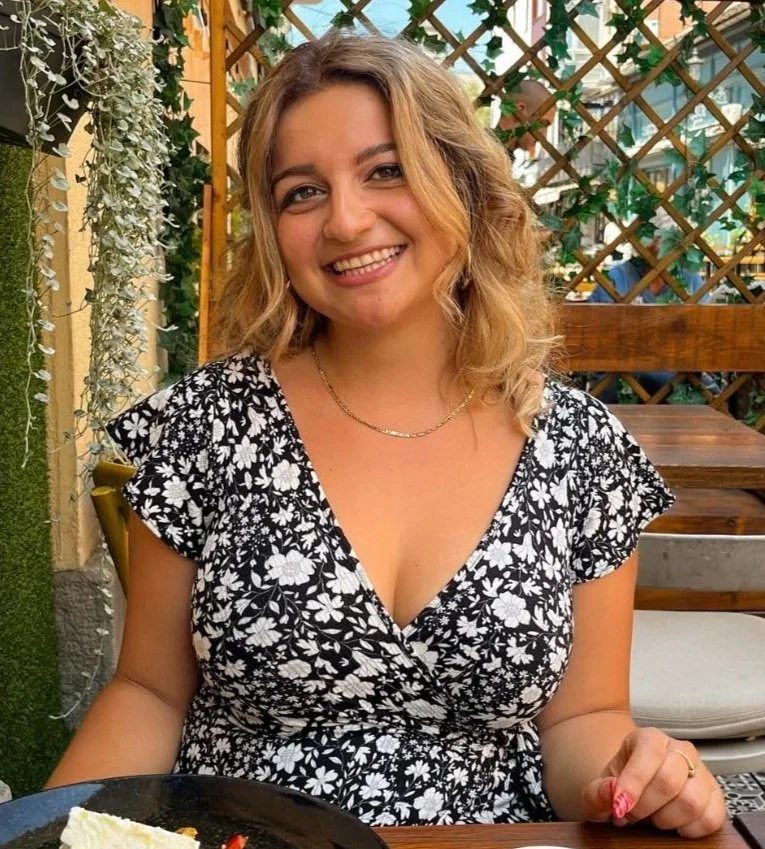 Aleks smiling outdoors at a restaurant table