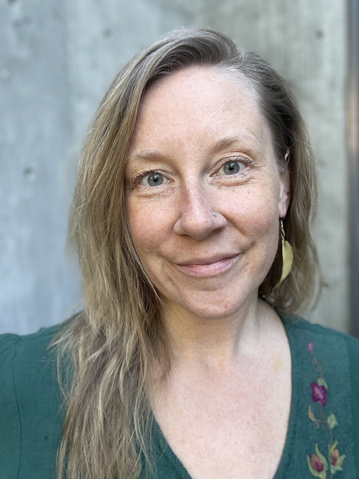 Juliana Christine smiling, wearing a green top with floral embroidery