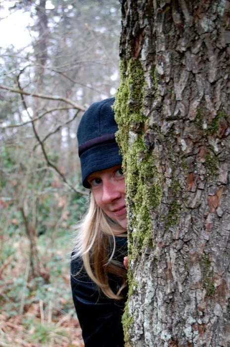 Juliana peeking from behind a moss-covered tree in a forest